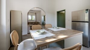 Un coin repas avec une table en bois, des chaises blanches et un réfrigérateur en acier inoxydable.