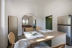 Ein Essbereich mit Holztisch, weißen Stühlen und einem Edelstahlkühlschrank.