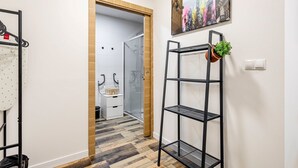 A hallway with a wooden door, a metal shelf with a plant, and a cityscape painting on the wall.