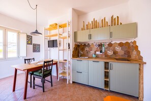 A compact kitchen with a dining area, featuring a wooden table, chairs, and a built-in TV. - Pazzariello Roof by NapoliApartments (Naples)