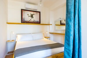 Une chambre d’hôtel avec un lit, des tables de chevet, un tableau, un appareil de climatisation et un miroir.