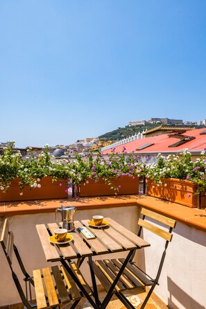 A terrace with a table and chairs, a view of buildings, and a hill in the background. - Pazzariello Roof by NapoliApartments (Naples)