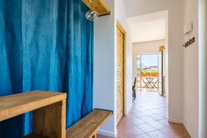 A hallway with a wooden bench, blue curtains, and a view of an outdoor balcony with a table and chairs. - Pazzariello Roof by NapoliApartments (Naples)