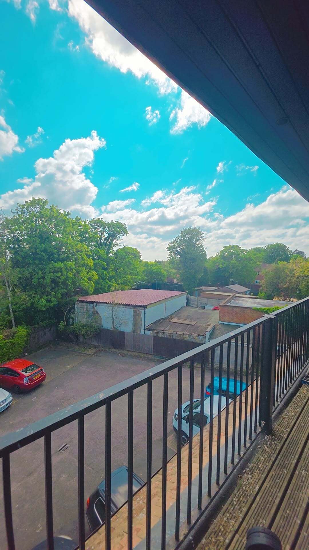 A balcony with a view of a parking lot, a swimming pool, and surrounding greenery.