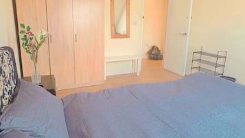 A bedroom with a bed, wardrobe, mirror, bench, and a small shelf.
