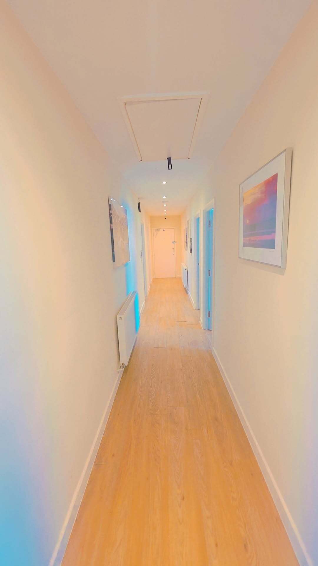 A hallway with wooden flooring, white walls, and doors on both sides.