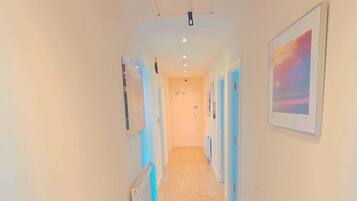 A hallway with wooden flooring, white walls, and doors on both sides.