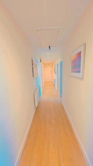 A hallway with wooden flooring, white walls, and doors on both sides. - Heathrow ensuite rooms (Feltham)