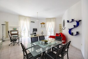 A modern living room with a glass dining table, black chairs, a red sofa, and a large blue number '2' decoration on the wall. - PizzArcHouse - One Bedroom Apartment, Sleeps 4 (Naples)