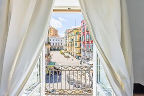 A view from a balcony with white curtains, overlooking a street with colorful buildings and a fountain. - PizzArcHouse - One Bedroom Apartment, Sleeps 4 (Naples)