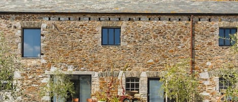 A stone building with a water tank on the roof, a gravel driveway, and potted plants.