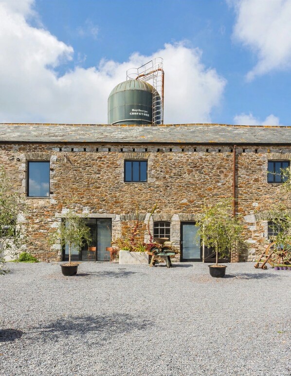 A stone building with a water tank on the roof, a gravel driveway, and potted plants.