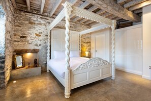 A four-poster bed with intricate carvings, a stone wall, and a wooden ceiling.