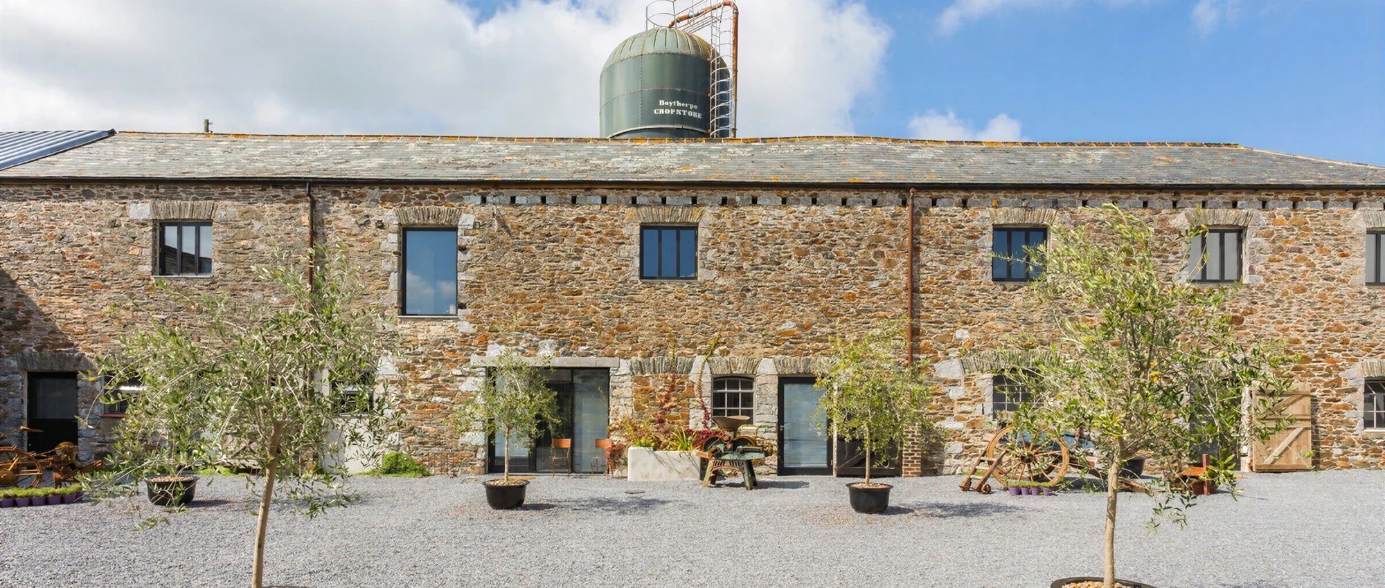 A stone building with a water tank on the roof, a gravel courtyard, and potted plants.