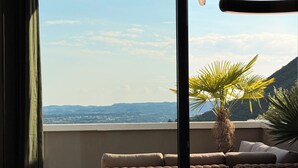 Een balkon met uitzicht op verre heuvels, een rieten zithoek en een tafel.