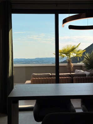 A balcony with a view of distant hills, a wicker sofa, and a table. - Deluxe Sky Spa Penthouse & Resort (Toscolano Maderno)