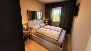 Un dormitorio con cama, mesita de noche, lámpara, espejo y ventana con cortinas.