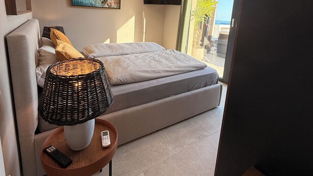 Un dormitorio moderno con cama, televisor, un cuadro y vistas al exterior.