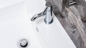 Ett badrum med ett vitt handfat, ett kromfärgat blandare och en väggbeklädnad av marmor bakom handfatet.