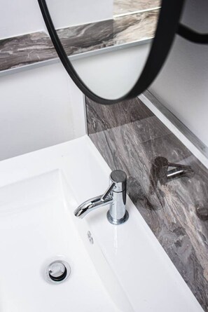 A bathroom with a white sink, chrome faucet, and a marble backsplash. - Treetop View by MyCityHaven (Redland)