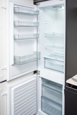 An open refrigerator with multiple transparent shelves and a freezer compartment below. - Treetop View by MyCityHaven (Redland)