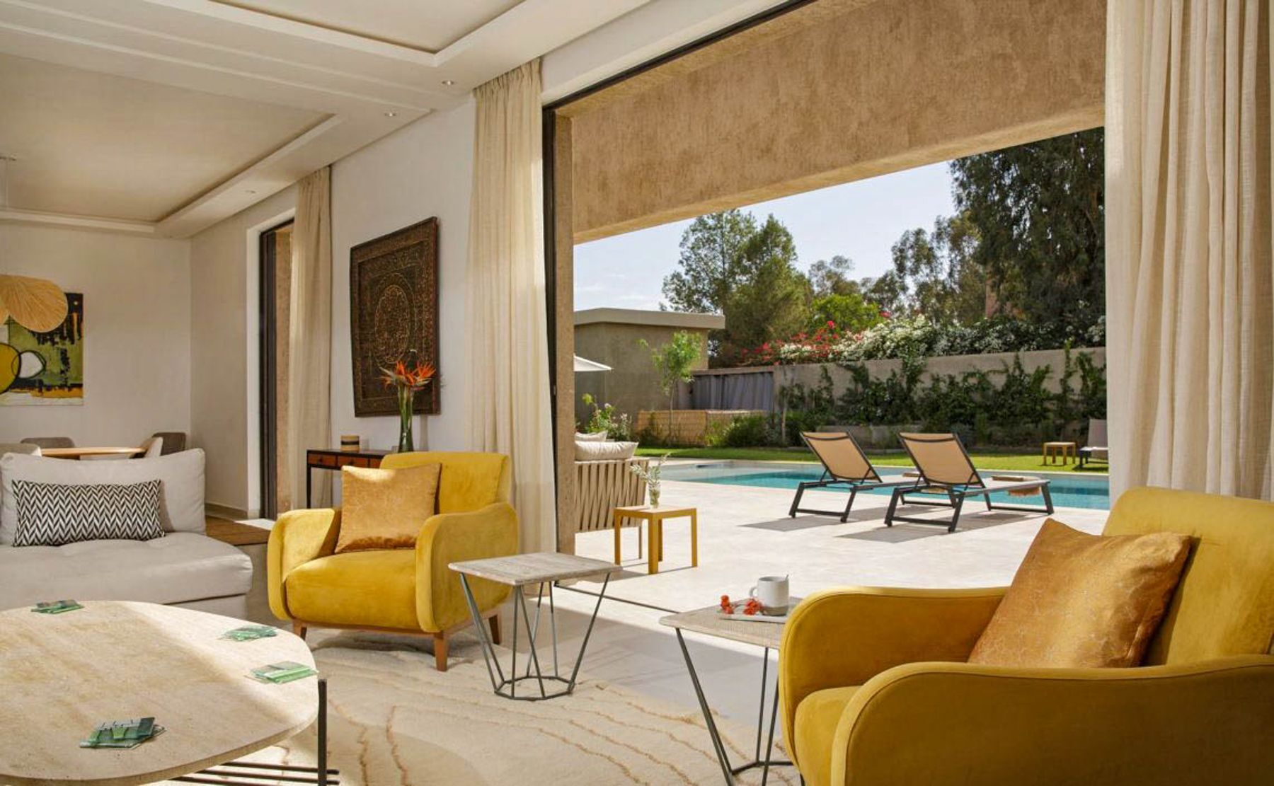 A modern living room with yellow sofas, a coffee table, and a view of a swimming pool.