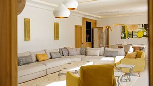 A modern living room with a sectional sofa, a yellow armchair, and a dining area with a table and chairs. - Villa Dalaoui - Five Bedroom Villa, Sleeps 10 (Douar Moulay Abbas)