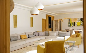 Ein modernes Wohnzimmer mit einem Ecksofa, einem gelben Sessel und einem Essbereich mit Tisch und Stühlen.