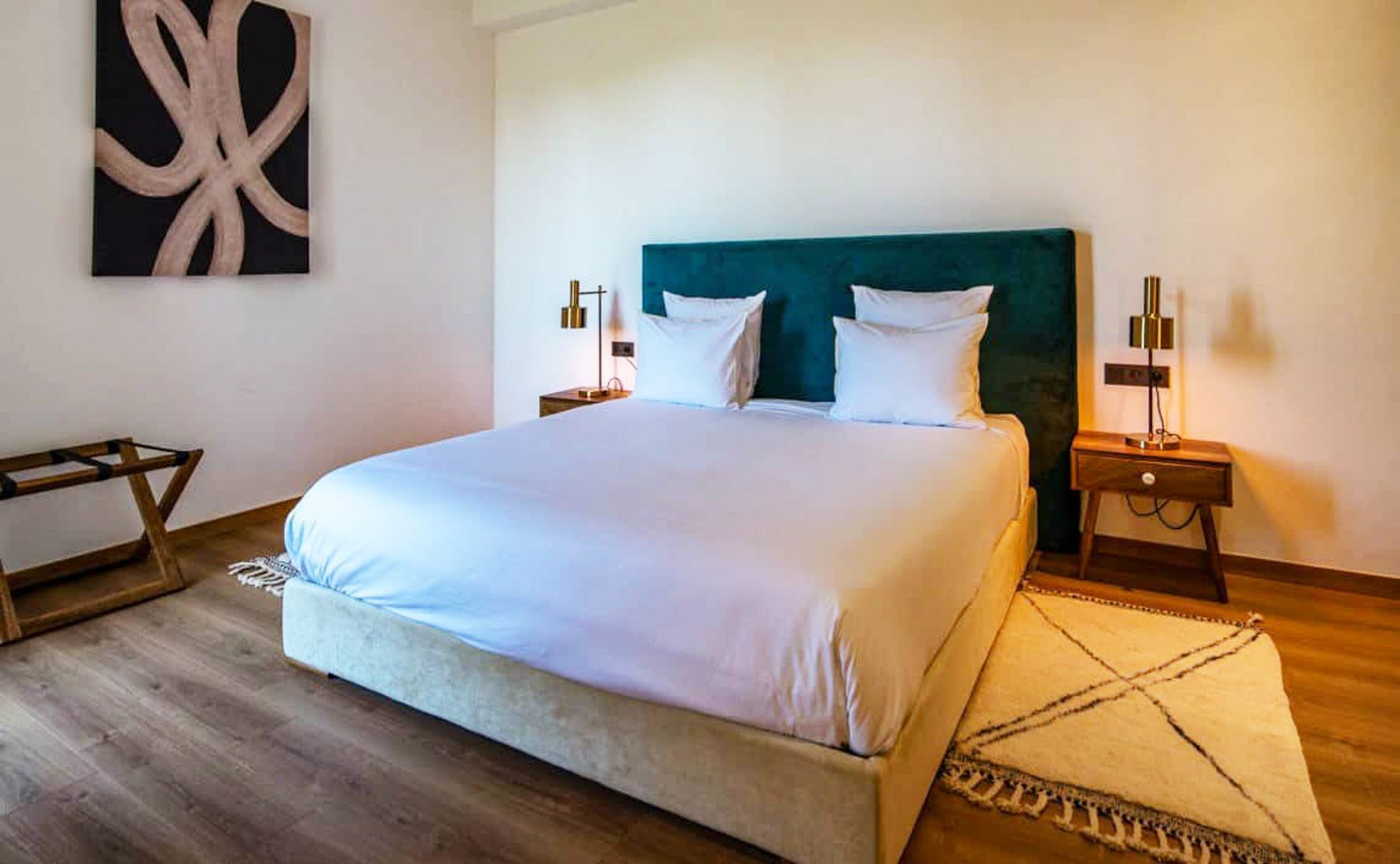 Una cama bien hecha con sábanas blancas, un cabecero azul turquesa y dos mesitas de noche con lámparas.