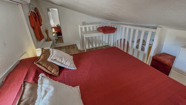 Ein Schlafzimmer mit roter Bettdecke, weißen Kissen, einem weißen Babybett und einer weißen Kommode.