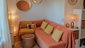 Ein gemütliches Wohnzimmer mit einer Couch, einem runden Spiegel, einer Wanduhr und einer Lampe.