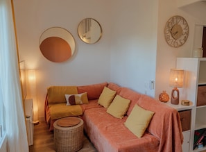 Ein gemütliches Wohnzimmer mit einer Couch, einem runden Spiegel, einer Wanduhr und einer Lampe.