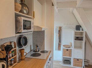 A kitchen with a microwave, stove, and various kitchen utensils. There is a wooden countertop and a white cabinet. - Charming studio with terrace near the beaches (Hyères)
