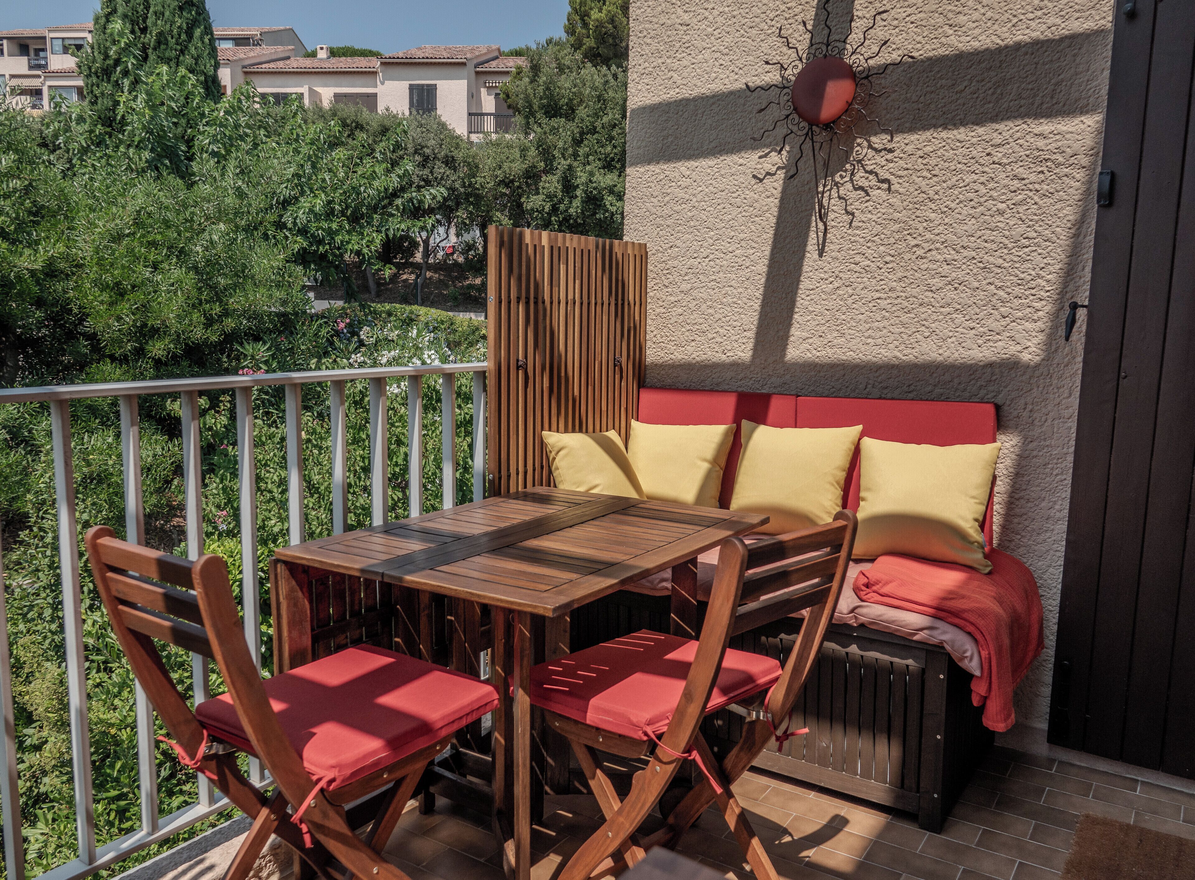 An outdoor patio with a wooden table and chairs, a red cushioned bench, and a decorative wall feature.