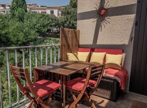Un patio al aire libre con una mesa y sillas de madera, un banco rojo con cojines y un elemento decorativo en la pared.