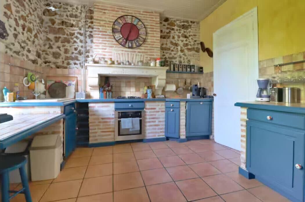 A kitchen with blue cabinets, a brick wall, a clock, and a tiled floor.