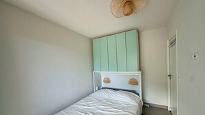 Un dormitorio con cama, cabecera verde claro, pared blanca y una puerta.