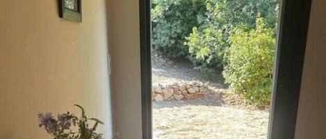 Un dormitorio con dos camas, una mesita de noche con un jarrón y vistas a un jardín exterior.