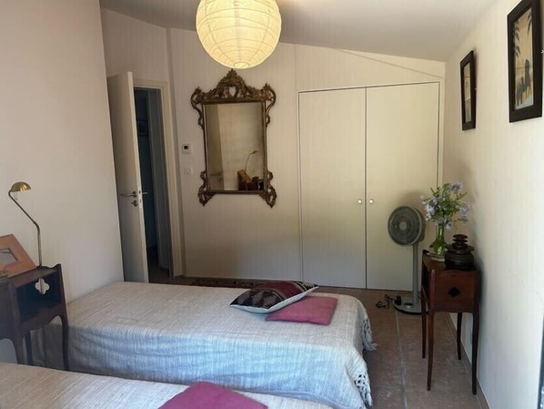 Une chambre avec deux lits, une armoire, un miroir, une table de chevet et une lampe.