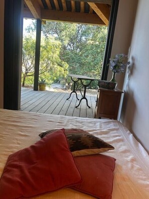 A bedroom with a bed, a red pillow, a small table with a vase, and a view of an outdoor deck. - Villa with pool and panoramic views in Ollioules (Ollioules)