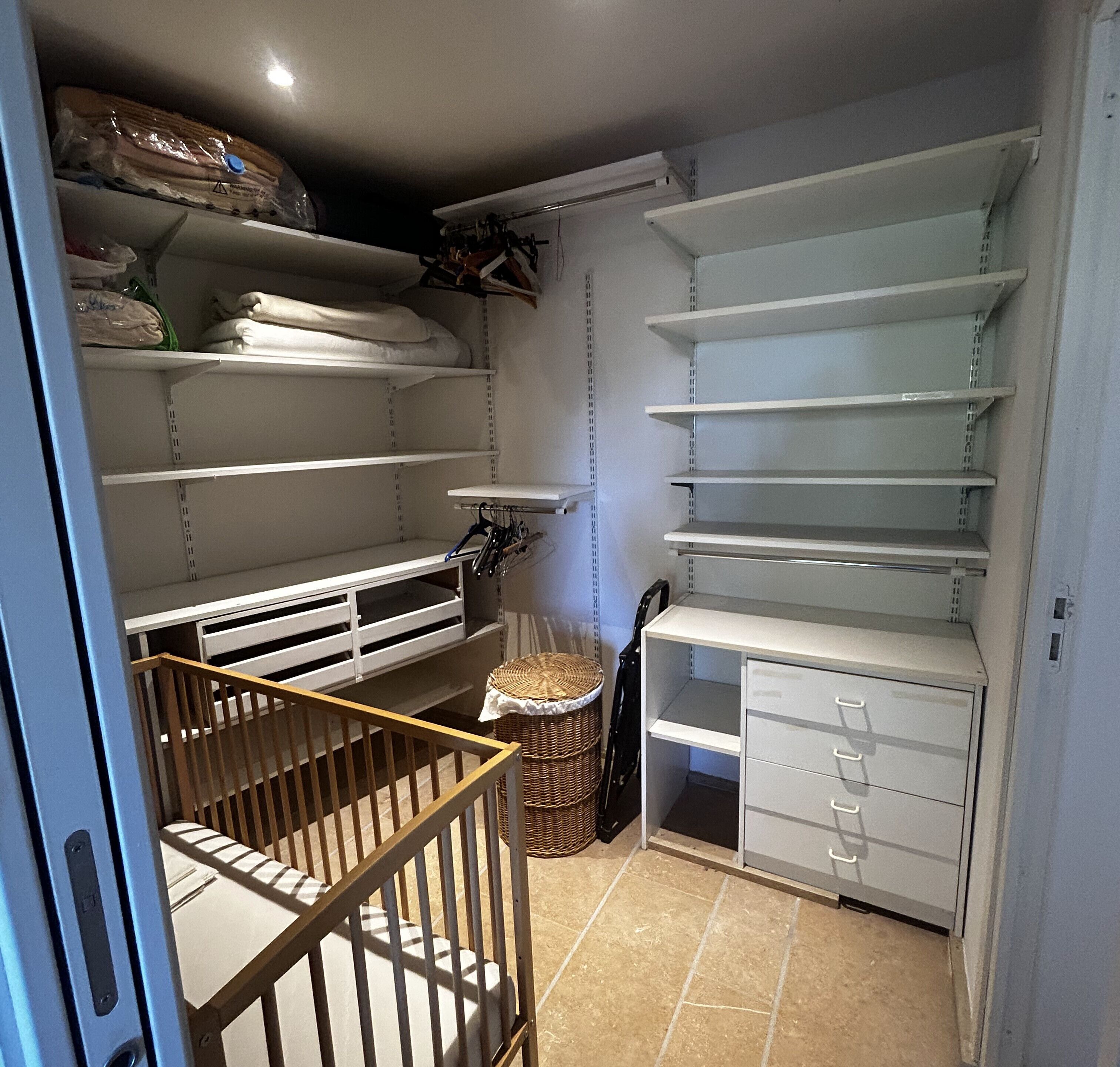 A storage room with shelves, a wicker basket, and a baby crib.