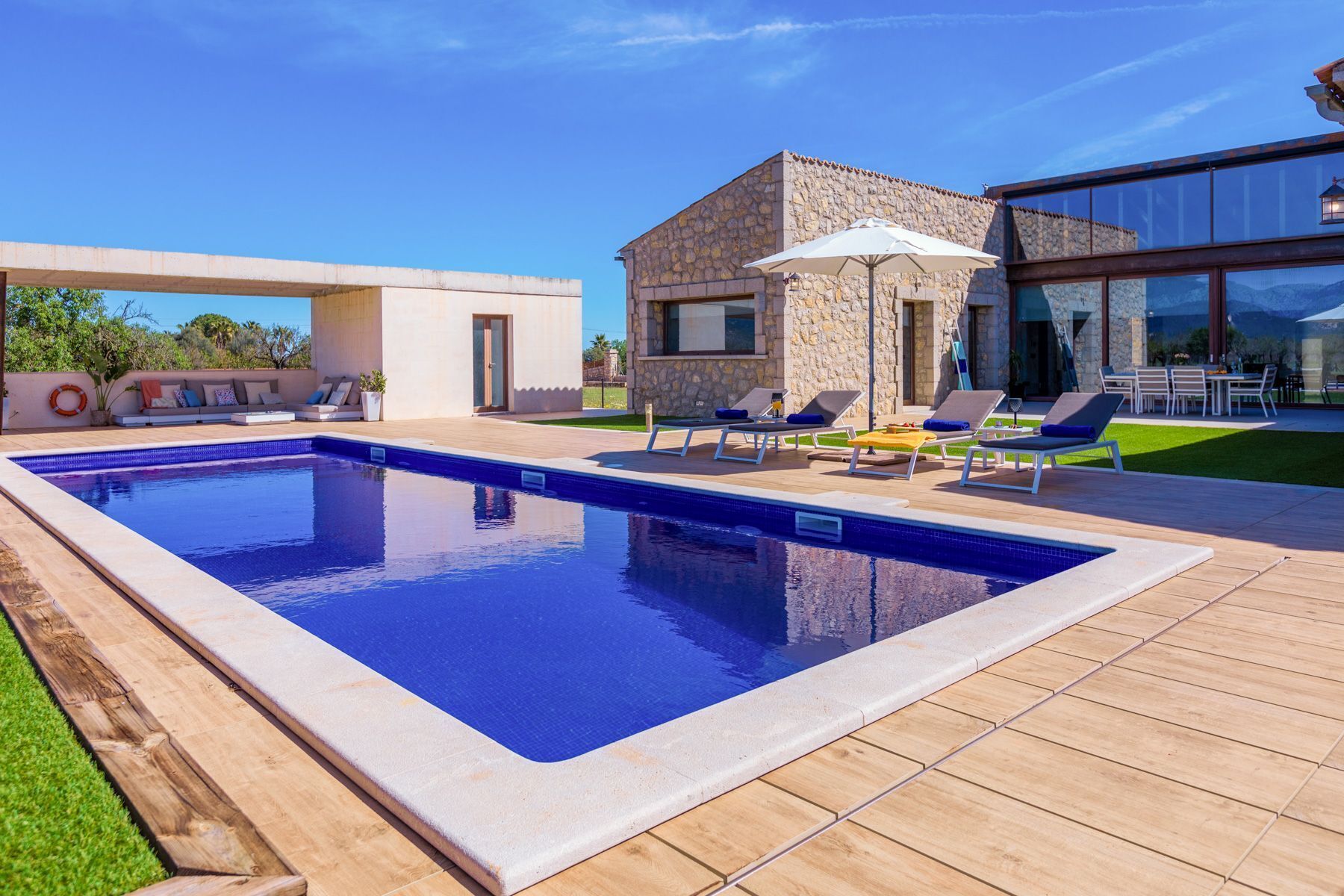 Un espace piscine extérieur moderne, avec un bâtiment en pierre, des chaises longues et un ciel dégagé.
