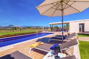 Ein Poolbereich mit Liegestühlen, einem Tisch mit einem Getränk und einem großen Sonnenschirm.