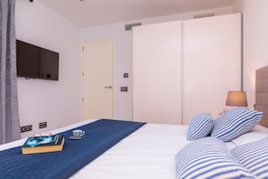A hotel room with a bed, a television mounted on the wall, a door, and a bedside table with a lamp. - Villa Pareteta - Three Bedroom Villa, Sleeps 6 (Binissalem)