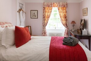 A bedroom with a bed, a radiator, a desk with a lamp, and a window with curtains.
