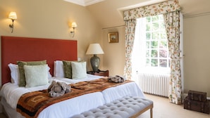 Habitación de hotel con una cama grande, un banco, una mesita de noche, una lámpara, una ventana con cortinas y un radiador.