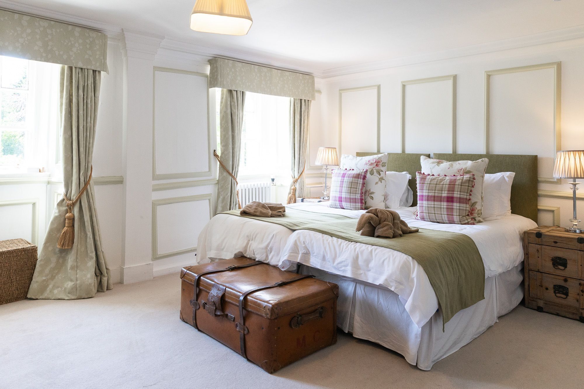 Een keurig opgemaakte slaapkamer met een groot bed, nachtkastjes, een lamp en een koffer.