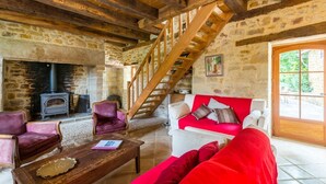 Ein rustikaler Innenraum mit Steinwänden, einer Holztreppe, einem Kamin und einem roten Sofa.