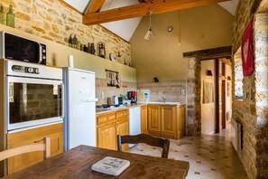 Uma cozinha rústica com paredes de pedra, armários de madeira, uma mesa de jantar e um micro-ondas.