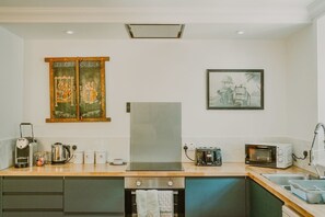 A modern kitchen with a refrigerator, microwave, toaster, and kettle. There are cabinets and a sink.